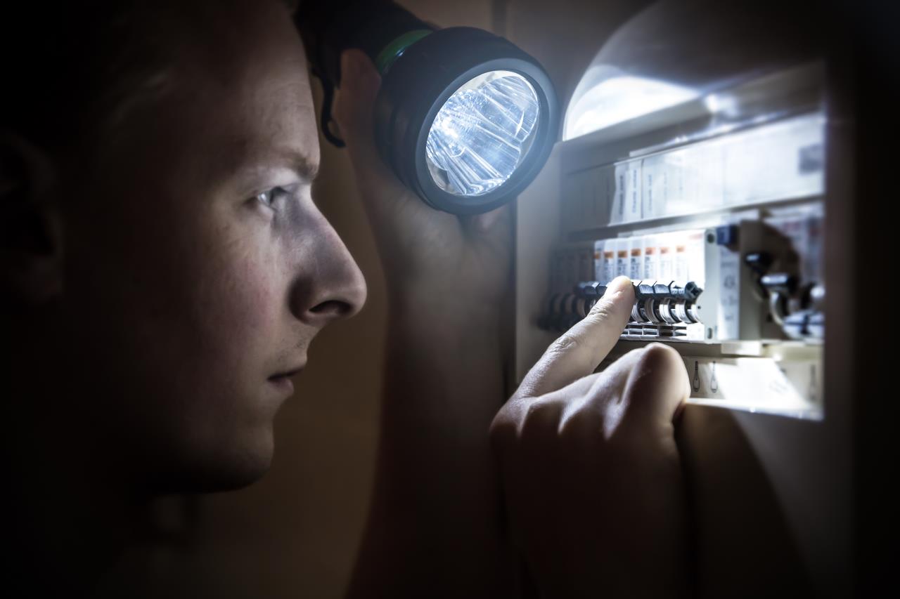 Guy looking at breaker with flashlight